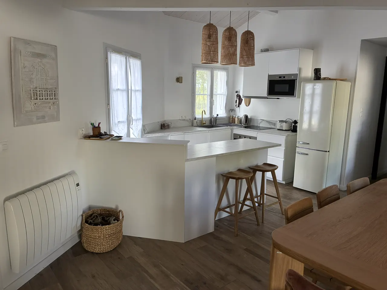 La cuisine ouverte, blanche, avec son bar et ses suspensions en rotin
