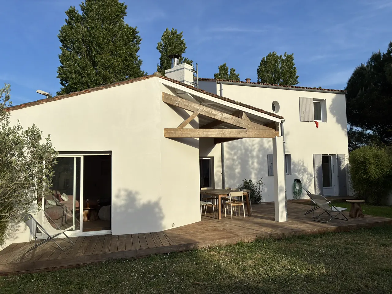 La maison côté jardin : murs blancs, pergola en bois, terrasse et pelouse