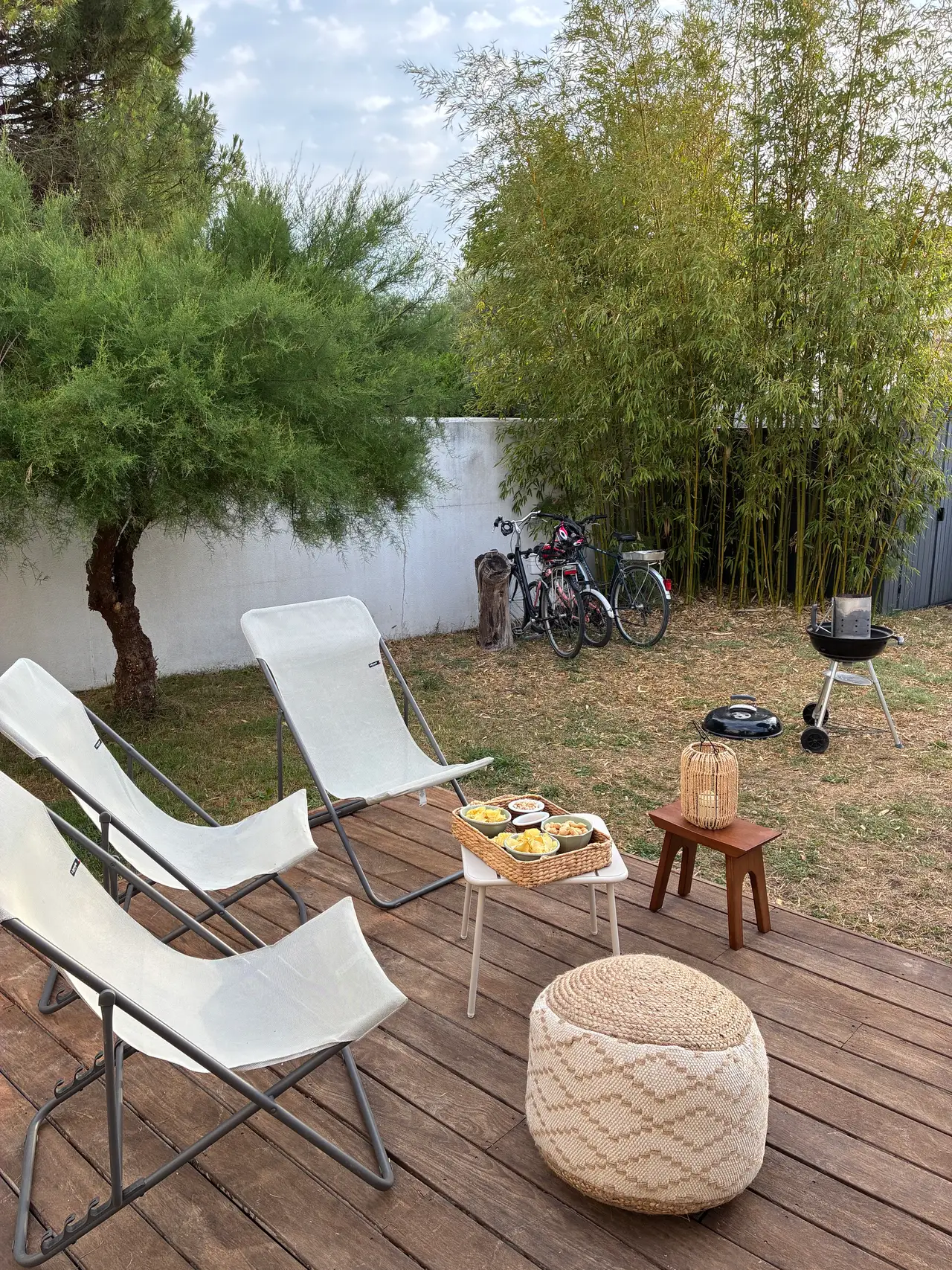 L’apéritif sur la terrasse : trois transats, un pouf, une lanterne, le barbecue et les vélos au fond du jardin devant les bambous